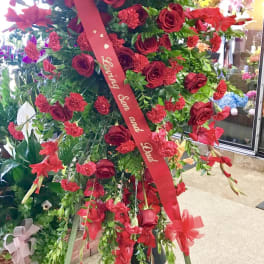 Large standing floral spray of red roses and carnations with a red ribbon