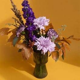 Purple and lavender flowers arranged in a green vase with autumn leaves