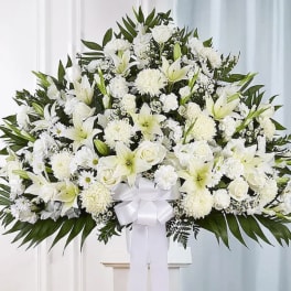 Large white funeral spray with lilies, roses, and chrysanthemums on a stand