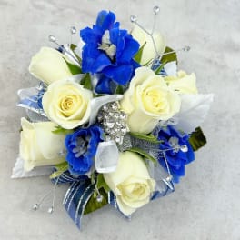 White roses and blue flowers arranged with silver ribbon and jeweled accents