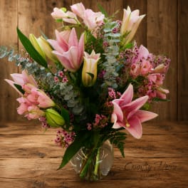 Pink lilies and small pink flowers arranged in a clear glass vase