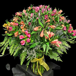 Pink and peach alstroemeria bouquet in a glass vase with a yellow ribbon