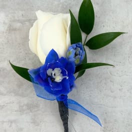White rose boutonniere with blue flowers and green leaves