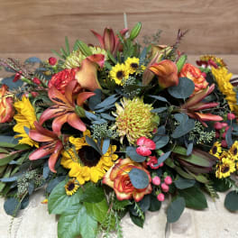 Low floral centerpiece with orange lilies, roses, and yellow sunflowers