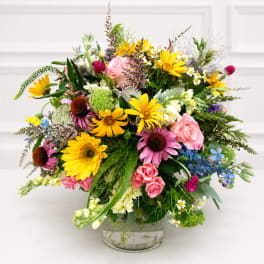 Mixed bouquet of yellow, pink, purple, and white flowers in a clear glass vase