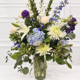 Mixed bouquet of white, blue, and purple flowers in a clear glass vase