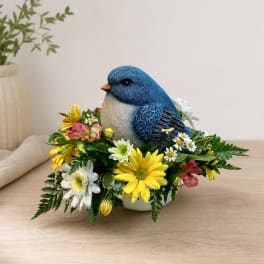 Blue bird figurine surrounded by yellow and white flowers in a low container