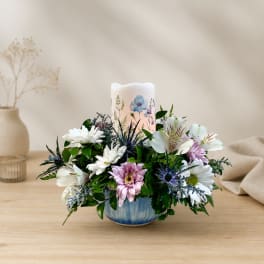 Mixed white and pink flowers arranged around a candle in a blue bowl