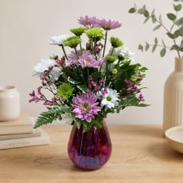 Mixed bouquet of purple, white, and green flowers in a magenta glass vase