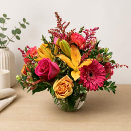 Bright mixed bouquet in a clear glass vase with pink, yellow, and orange flowers