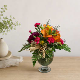 Mixed bouquet of orange, pink, and burgundy flowers in a glass vase