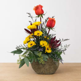 Red roses and yellow daisies in a round vase arrangement