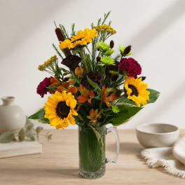 Sunflowers and mixed blooms arranged in a clear glass pitcher vase