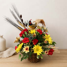 Basket arrangement with red and yellow flowers and a decorative bird topper