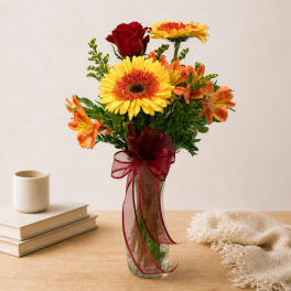 Mixed bouquet of yellow, orange, and red flowers in a glass vase with ribbon
