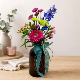 Colorful mixed bouquet in a dark glass vase with a teal ribbon