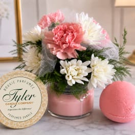 Pink and white flower arrangement in a glass vase with a candle tin and bath bomb