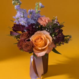Mixed bouquet of roses, carnations, and purple blooms in a vase with a ribbon