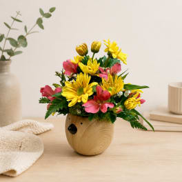 Yellow and pink flowers arranged in a small wooden bear-shaped vase