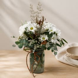 White daisy bouquet in a glass jar with a braided ribbon tie