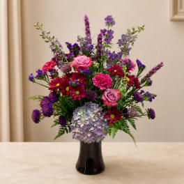 Mixed bouquet of pink, purple, and red flowers in a dark vase