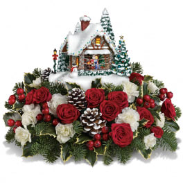 Christmas centerpiece with red roses, white carnations, and a snowy cottage decoration