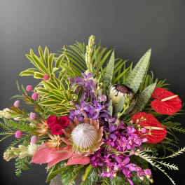 Tropical bouquet with purple orchids, red anthuriums, and a protea in a vase