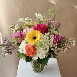 Mixed bouquet of roses, hydrangeas, and a yellow gerbera daisy in a glass vase