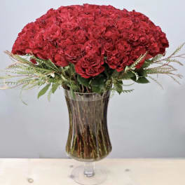 Tall bouquet of red carnations with feathery accents in a clear pedestal glass vase