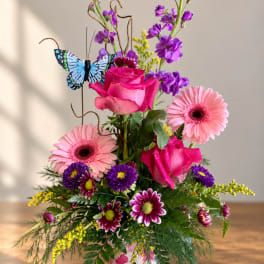 Pink roses and gerbera daisies in a butterfly-decorated vase with purple blooms