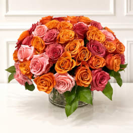 Bouquet of orange, pink, and red roses in a clear glass vase