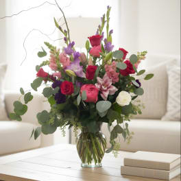 Mixed bouquet of roses, lilies, and purple flowers in a glass vase
