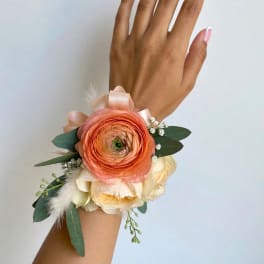 Peach and cream wrist corsage with ribbon and greenery on a hand