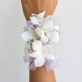 White floral wrist corsage with lavender ribbon on an arm