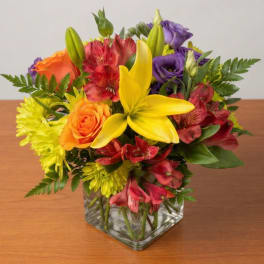 Mixed bouquet of lilies, roses, and alstroemeria in a clear square vase