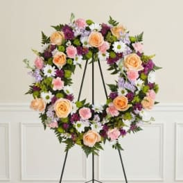 Floral wreath on a black stand with peach roses, daisies, and pink blooms