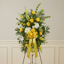 Yellow and white floral standing spray with a yellow ribbon on an easel
