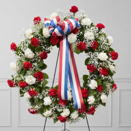 Red and white carnation wreath with a red, white, and blue ribbon bow