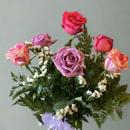 Bouquet of pink and lavender roses with white filler flowers and a purple ribbon