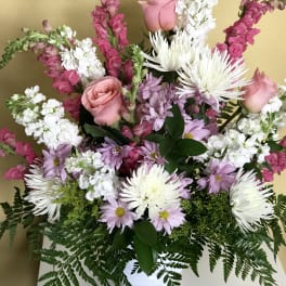 Mixed bouquet of pink roses, white chrysanthemums, and lavender daisies in a white vase