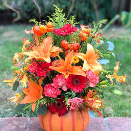 Autumn floral arrangement in a pumpkin-shaped container with orange lilies and red daisies
