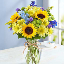 Bouquet of sunflowers, daisies, and purple flowers in a glass vase