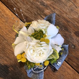 White rose corsage with yellow accents and silver ribbon on a wooden surface