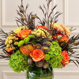 Mixed bouquet of orange roses, chrysanthemums, and green hydrangeas in a glass vase