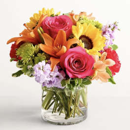 Mixed bouquet of roses, lilies, and sunflowers in a clear glass vase