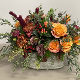 Low centerpiece of orange roses and rust mums with red accents in a gray ceramic container