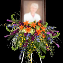 Standing floral spray with orange lilies and a framed portrait
