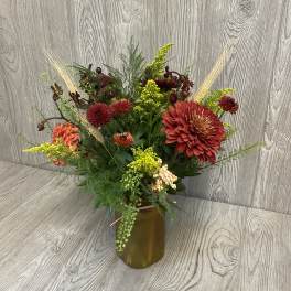Mixed autumn bouquet in an amber vase with red and orange blooms