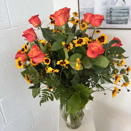 Bouquet of coral roses and yellow daisies in a clear glass vase