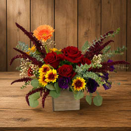 Mixed bouquet of red roses, orange gerbera daisies, and purple blooms in a wooden box